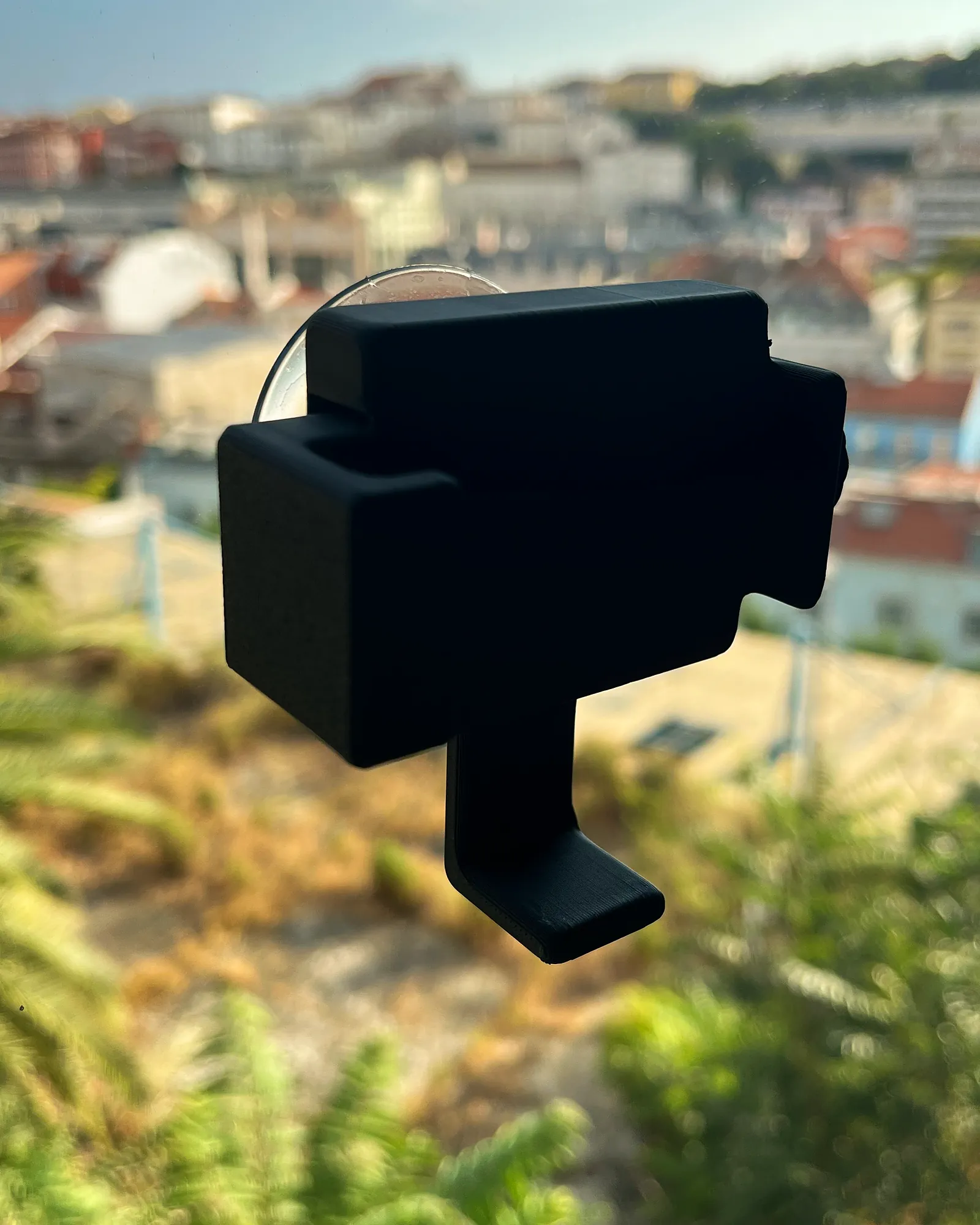 A Padel Holder attached by its suction cup to a pane of glass, with Lisbon rooftops out of focus behind it.